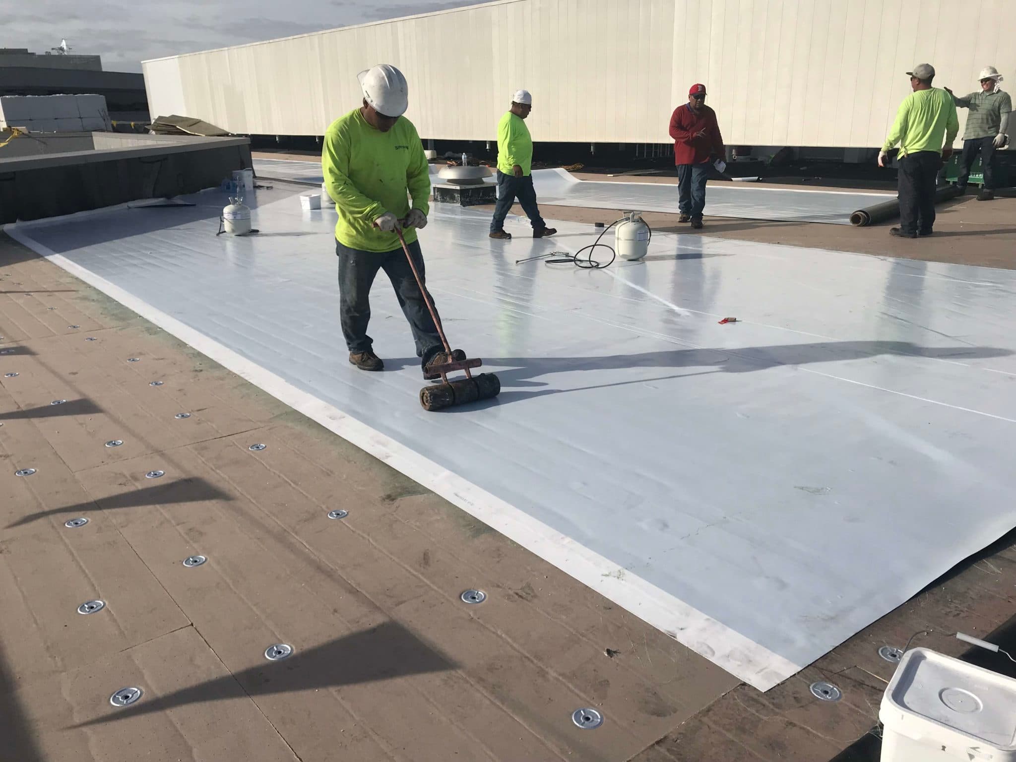 Crew rolling out white TPO membrane on a commercial flat roof