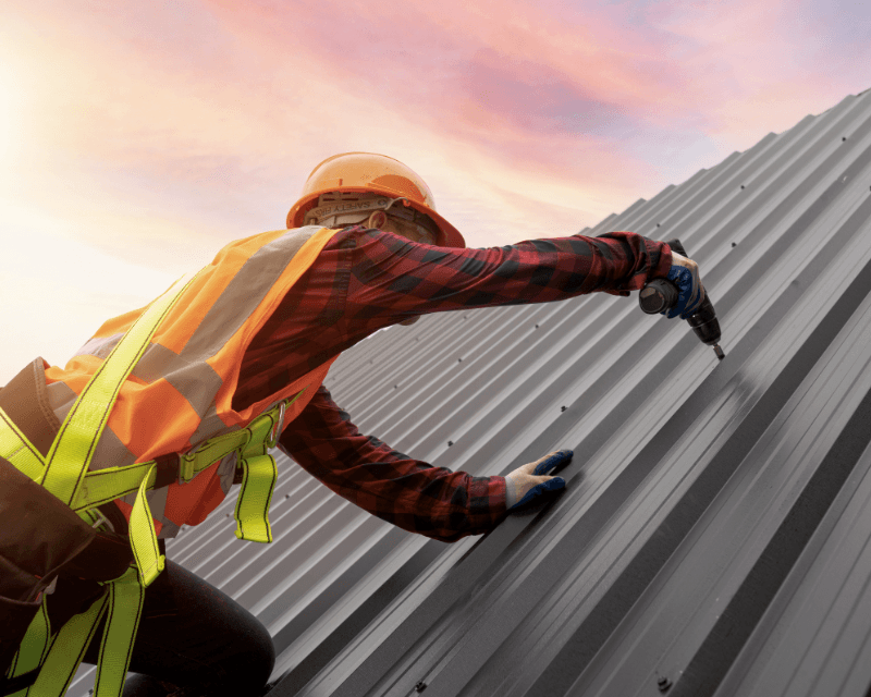 Crew member driving fasteners into a standing seam metal roof panel at sunset