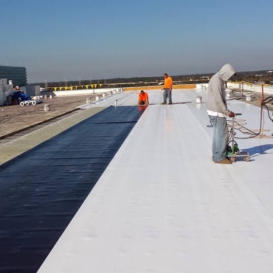 Crew installing white TPO membrane on a flat roof