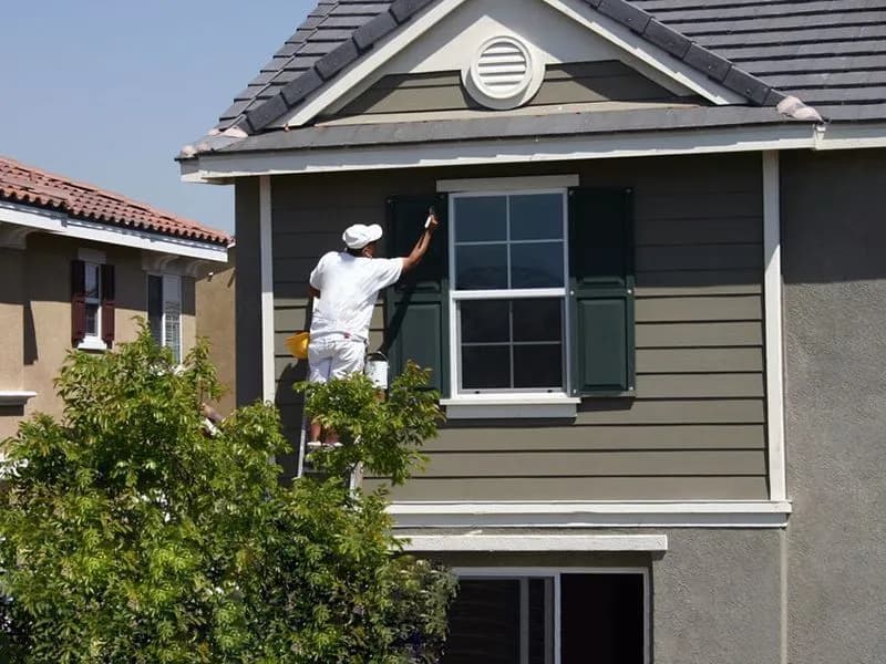 Painter on a ladder brush-cutting trim and shutters on a two-story home
