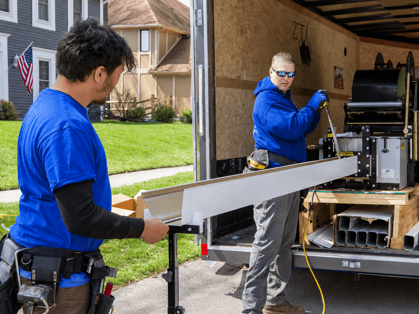 Two E4 crew members prepping seamless gutter material from the trailer-mounted fabrication rig