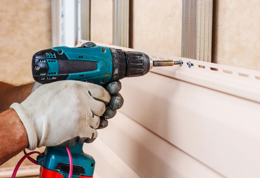Close-up of an E4 crew member driving a fastener into a new siding panel