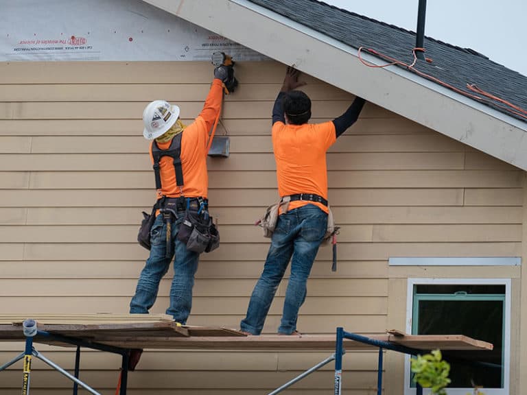 Two E4 crew members installing new siding on a gable wall