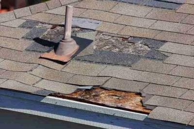 Close-up of damaged and missing shingles exposing the underlayment near a roof vent
