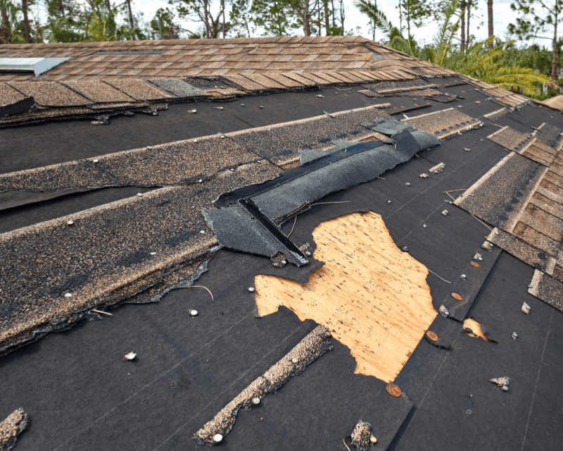 Aerial view of a storm-damaged roof with a patch of exposed plywood decking