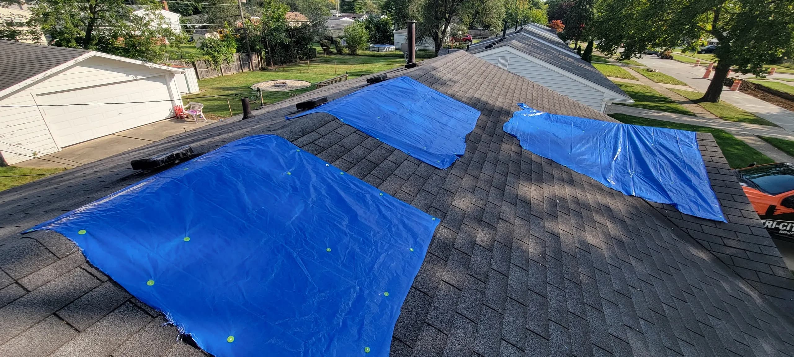 Aerial view of a neighborhood roof with three sections covered in blue emergency tarps