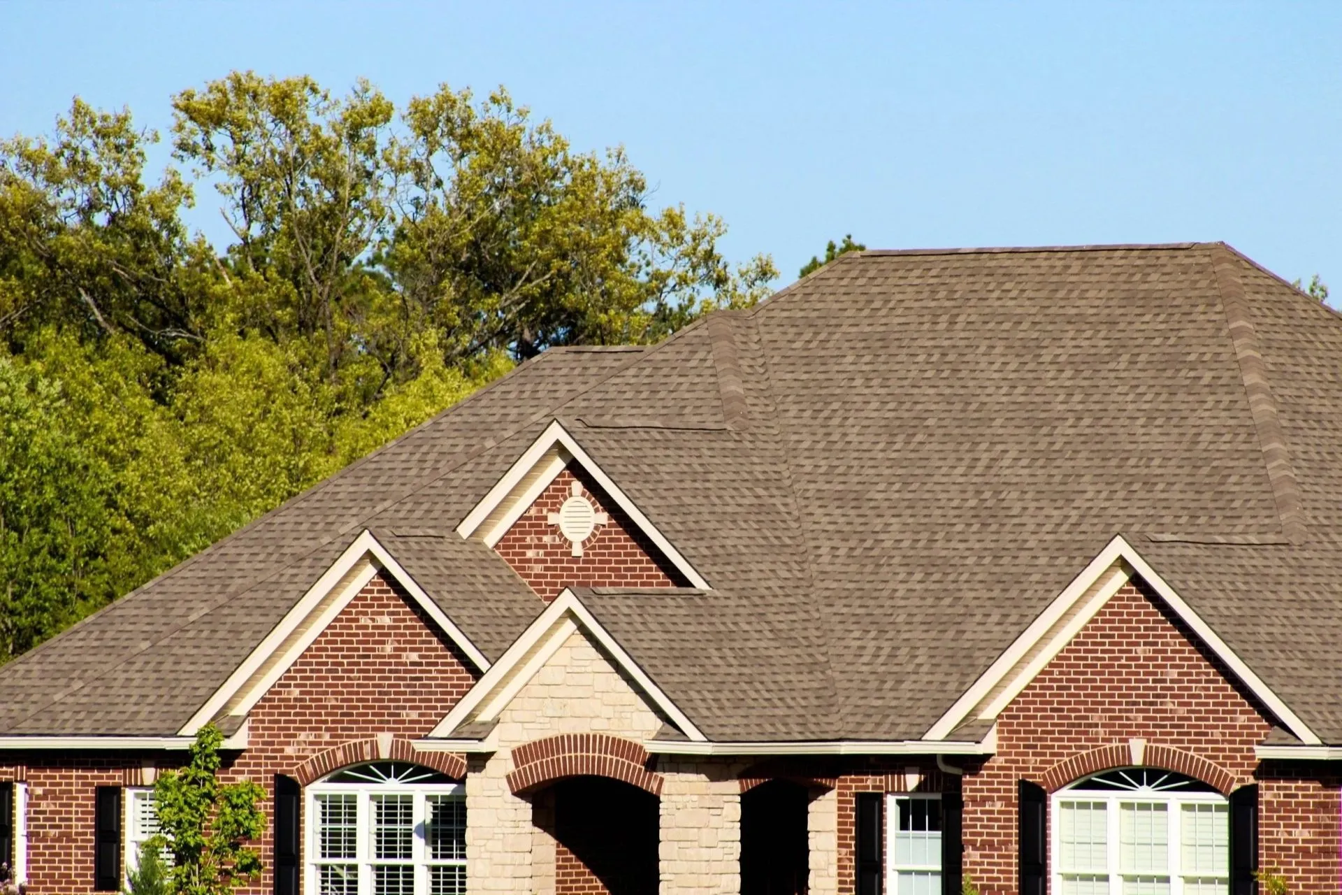 Close-up of a multi-gable brick home with a tan architectural shingle roof