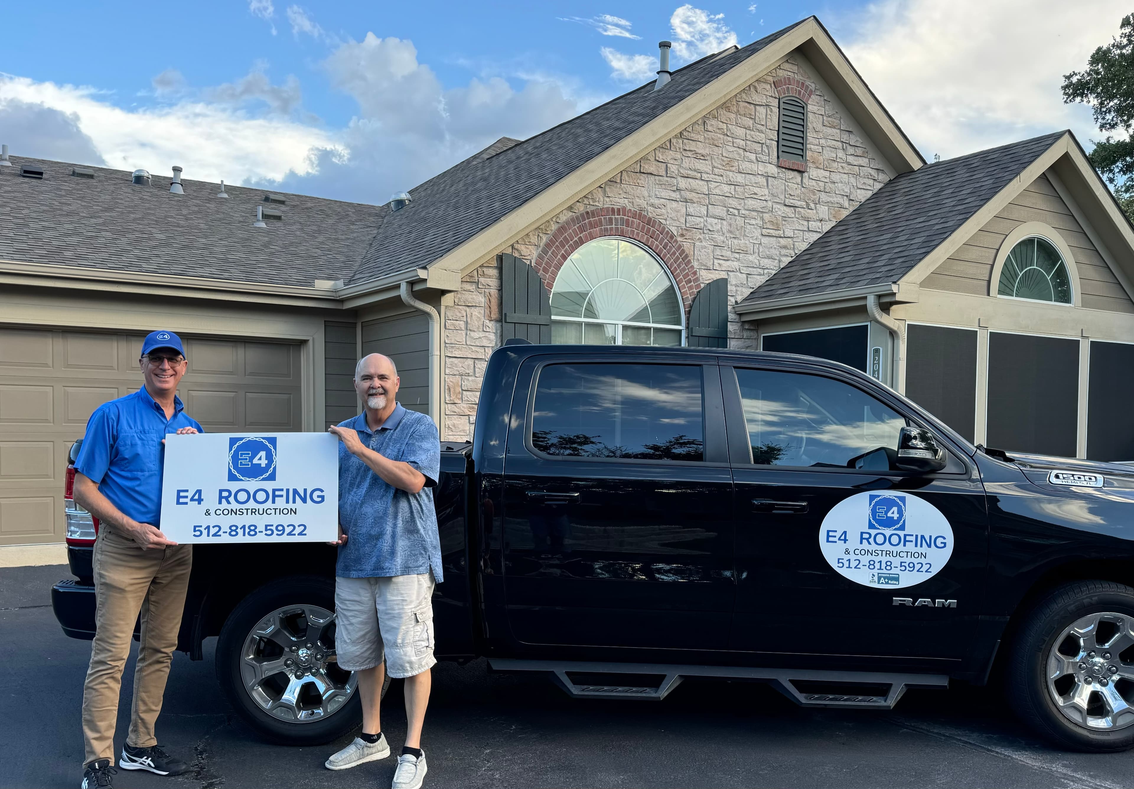 Two members of the E4 Construction team holding a company sign in front of their truck
