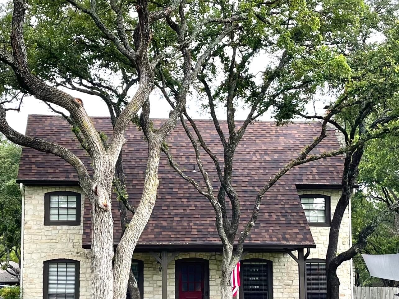Two-story stone home with a brown shingle roof and red front door