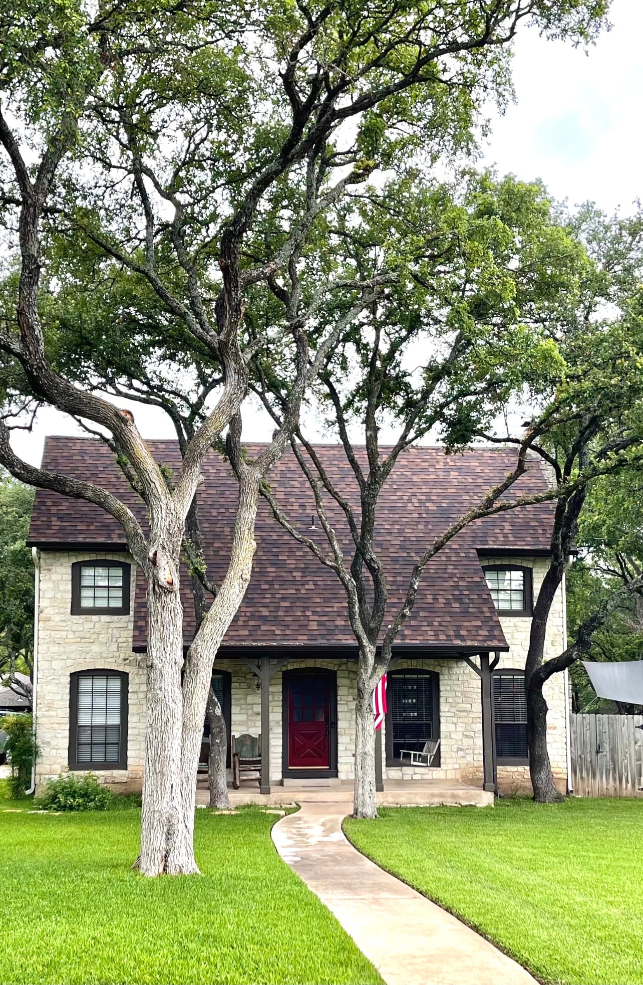 Two-story stone home with a brown shingle roof and red front door