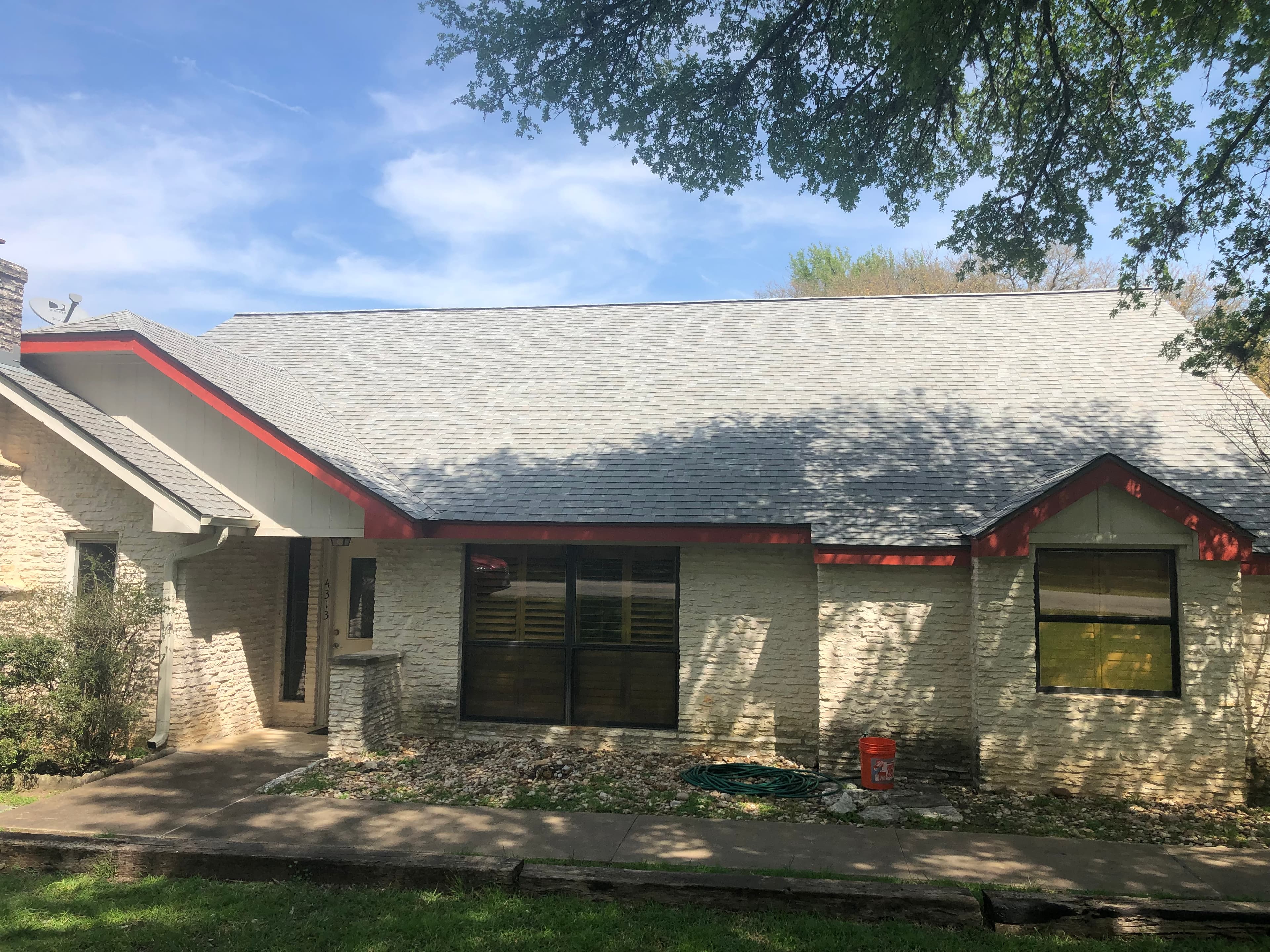 Light grey shingle roof with red-trimmed fascia on a stone Central Texas home