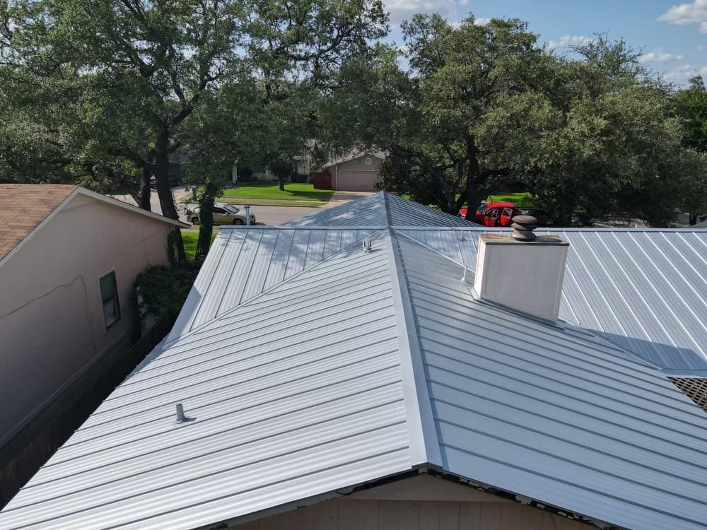 Aerial view of a light grey standing seam metal roof surrounded by mature trees