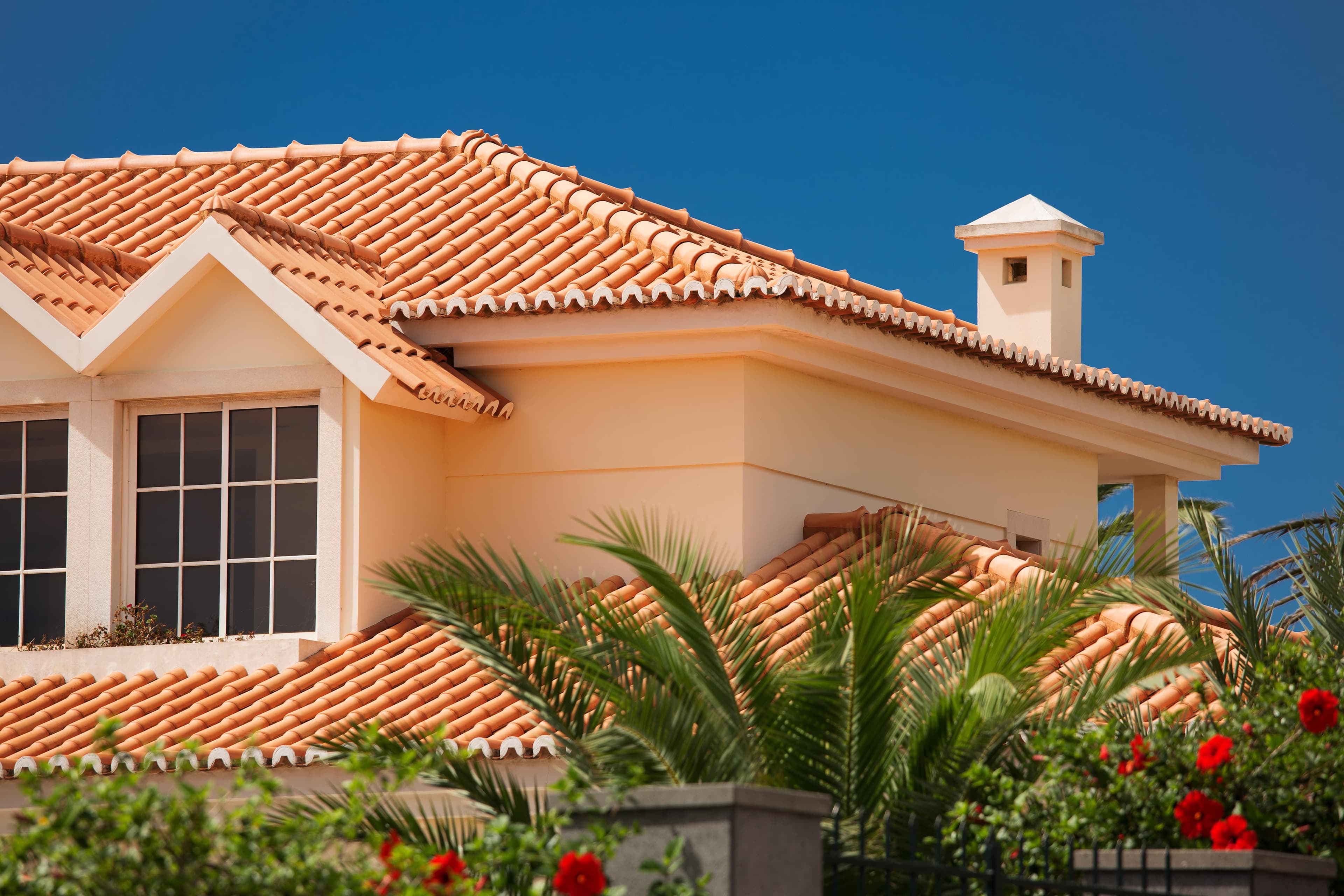 Terracotta clay tile roof on a Mediterranean-style stucco home under a clear blue sky