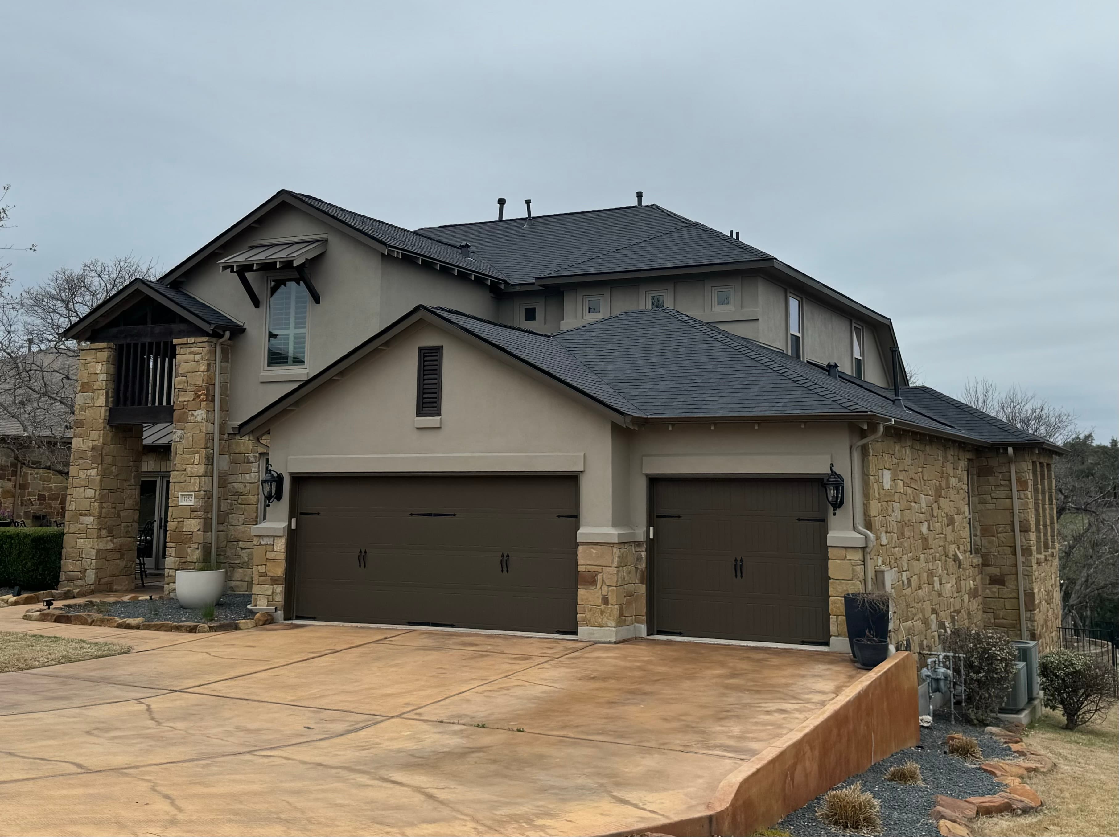 Two-story stone and stucco home with a dark grey architectural shingle roof and matching garage doors