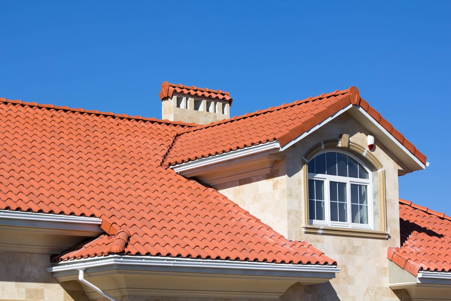 Terracotta clay tile roof on a stucco home under a clear blue sky